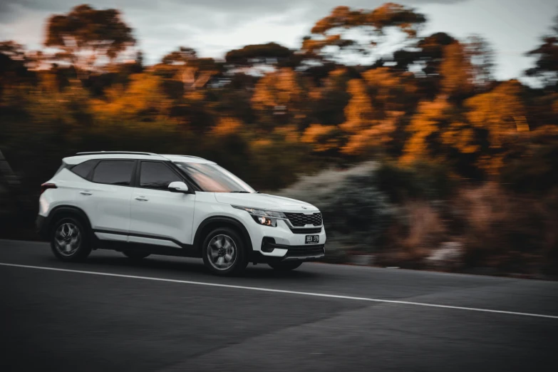 a white suv driving down a street next to trees