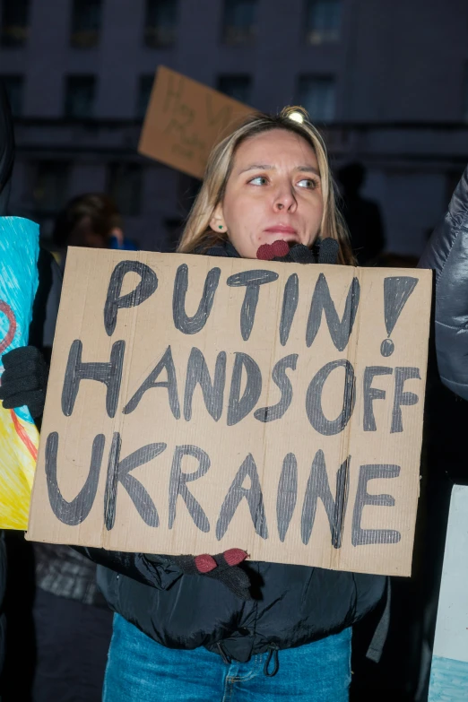 a woman in blue jeans holding a sign reading puttin'hands off ukraine