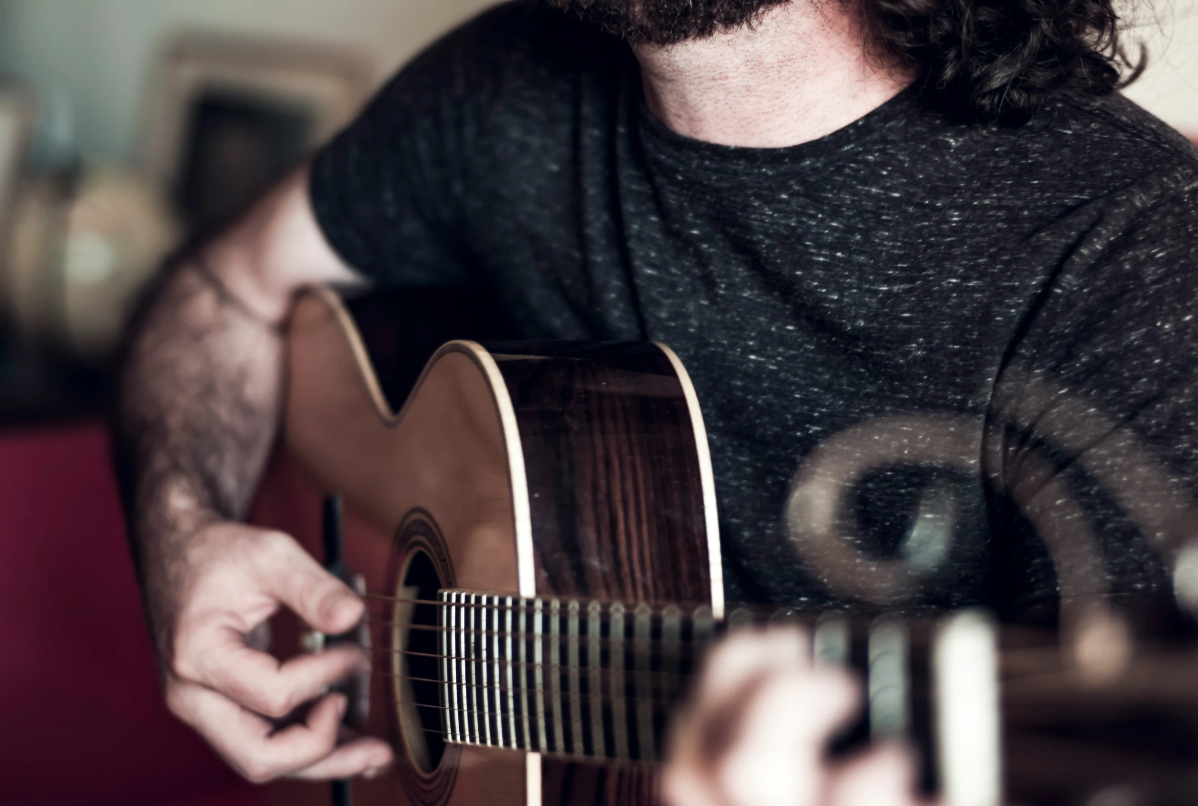 man playing guitar in front of window with one hand on the guitar