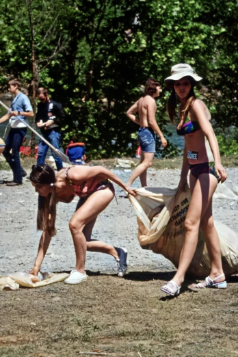 three girls in bikinis and hats are picking up a bag