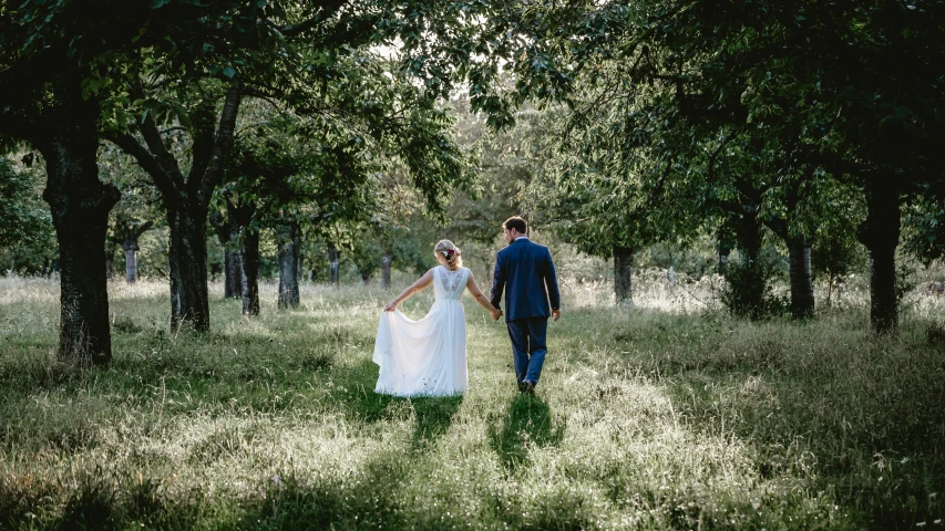 the bride and groom walking in an orchard near trees