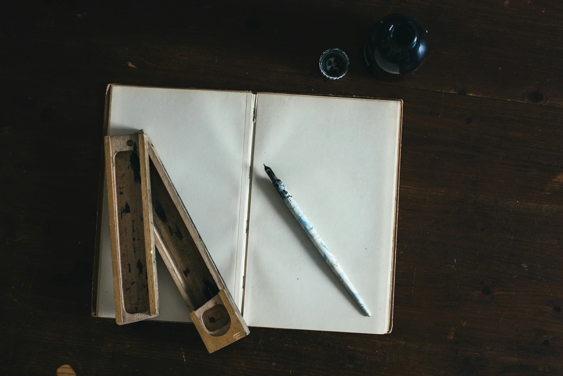 an open notebook on a wooden table with two pencils and ink