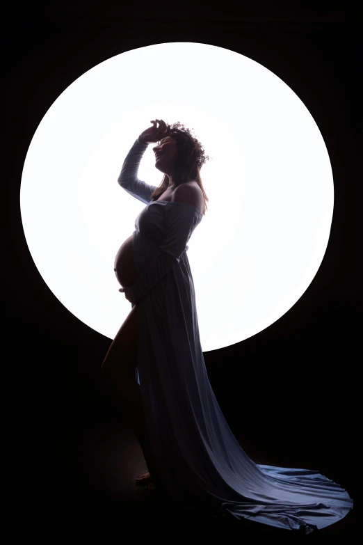 a pregnant woman in a dress and long veil stands in front of a white circle