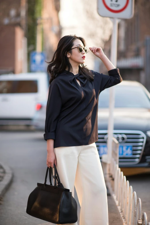 the woman is carrying a black handbag near a car