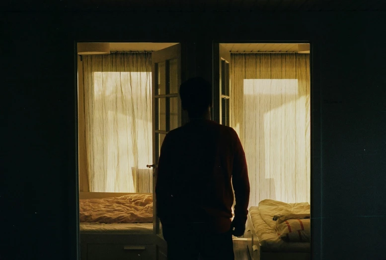 a person standing next to the door to the bed in the dark