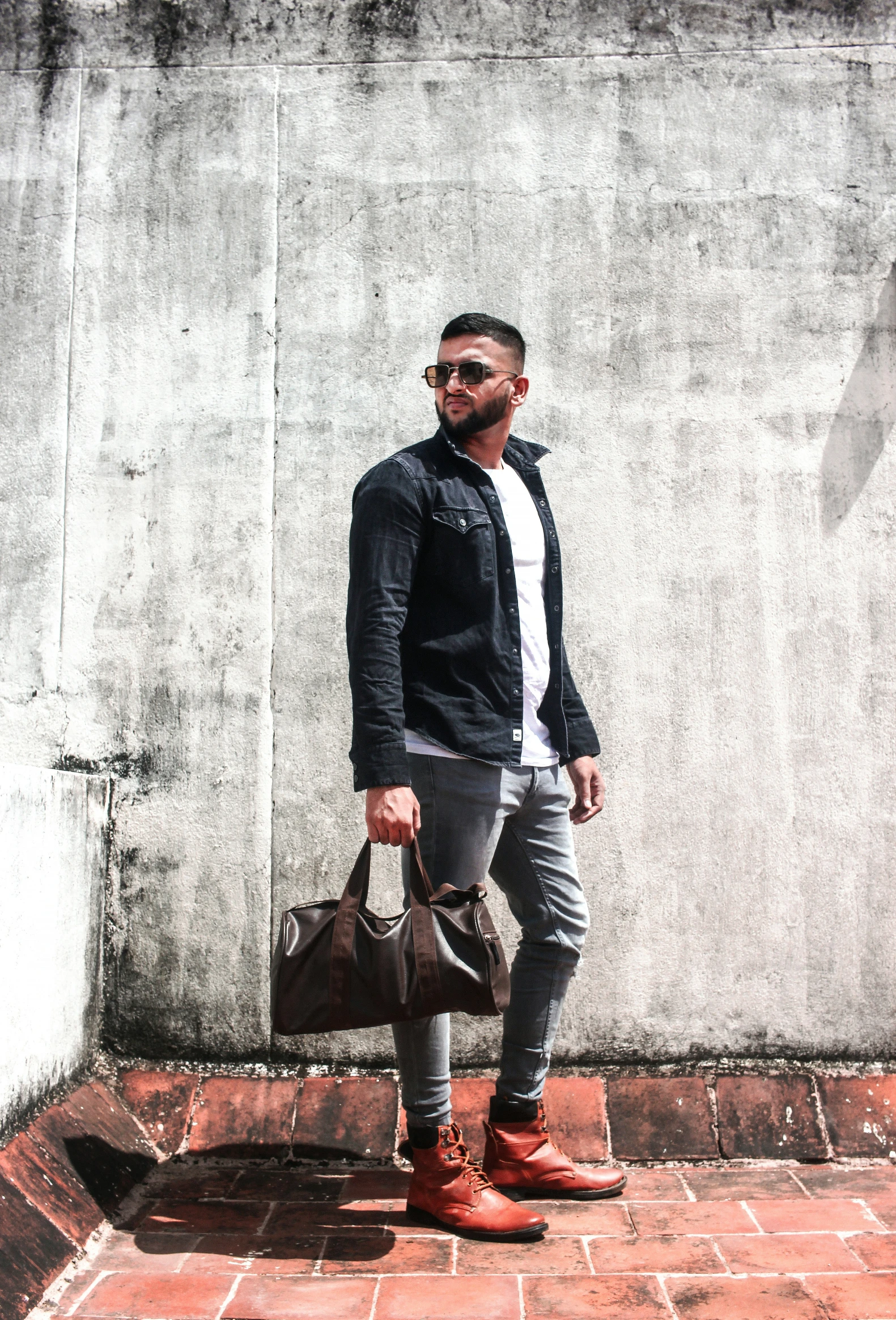 man standing on red tile near gray wall wearing sunglasses