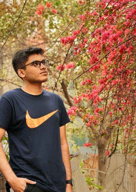 the man in the t - shirt is standing near a tree with red flowers