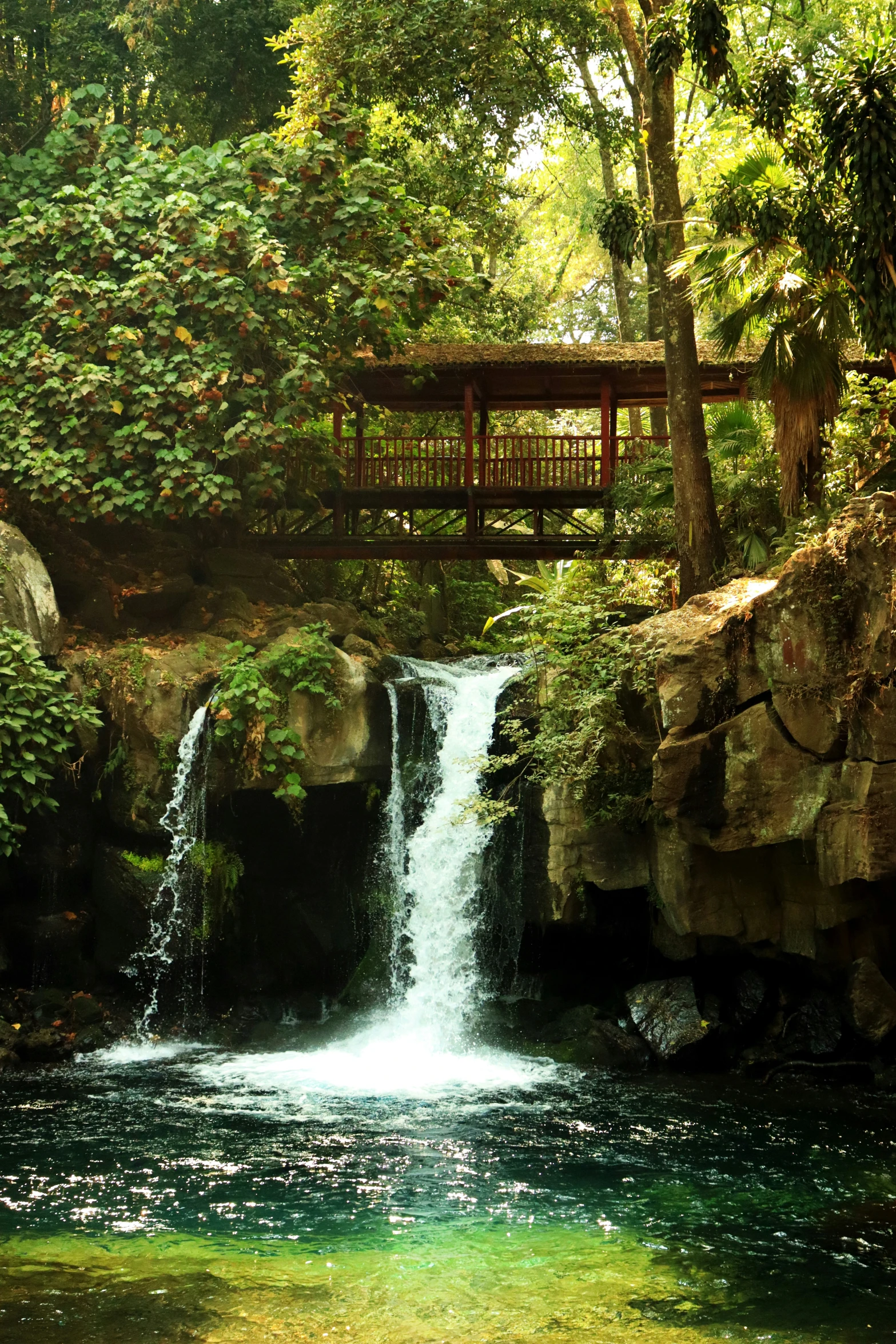 a large waterfall with a bridge above it near trees