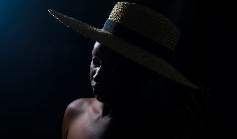 a man standing in front of a black wall wearing a straw hat