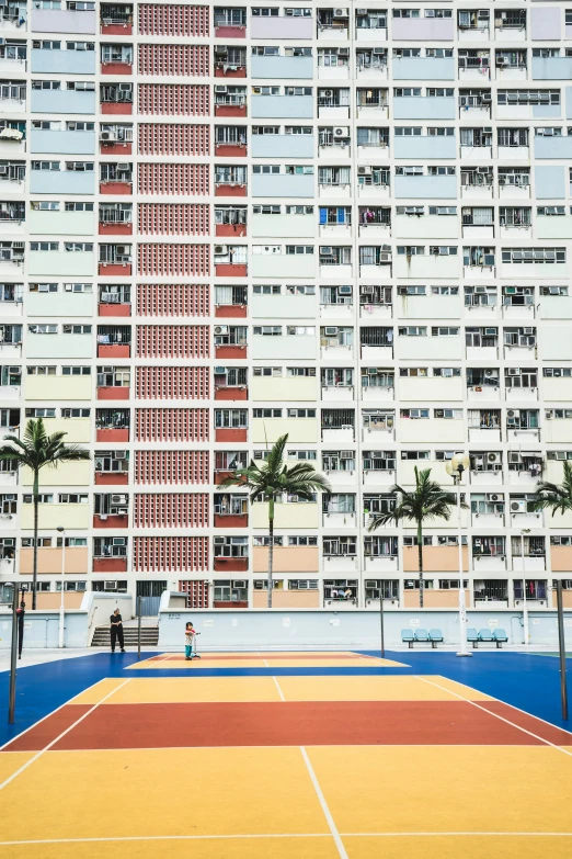 a tennis court with many windows, and an empty bench on the far side of it