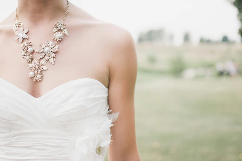 a woman in a wedding gown wears a flowered necklace