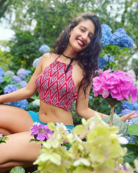 a woman sitting on the ground in a bikini top surrounded by flowers