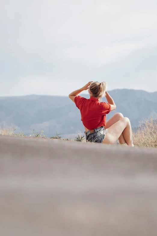 a woman is sitting in the grass on her knees with one hand on her head and wearing a hat