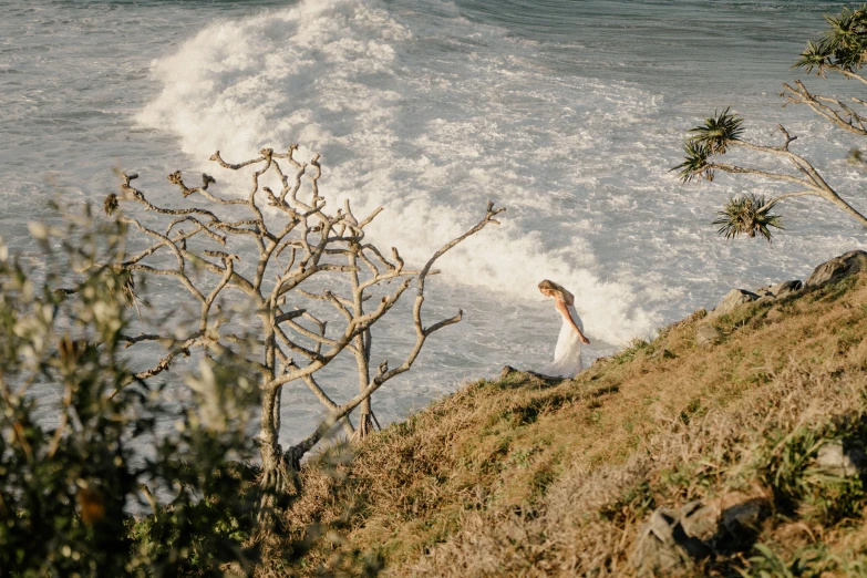 a woman is standing alone on a hill above the waves