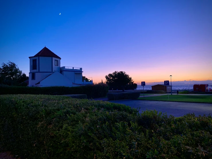 a small white building with a tower near a park at dusk