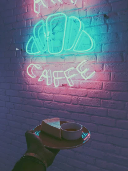 a hand is holding a coffee cup and a neon sign
