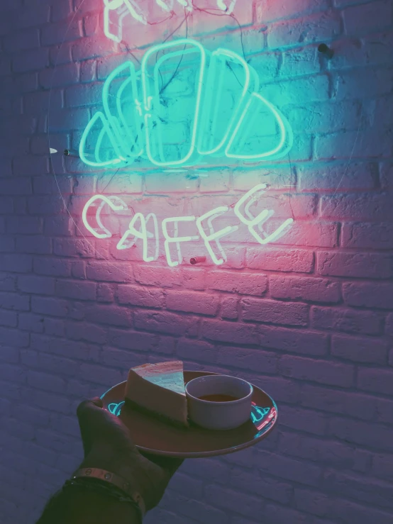 a hand is holding a coffee cup and a neon sign