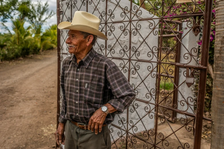 an older man wearing a cowboy hat standing by a fence