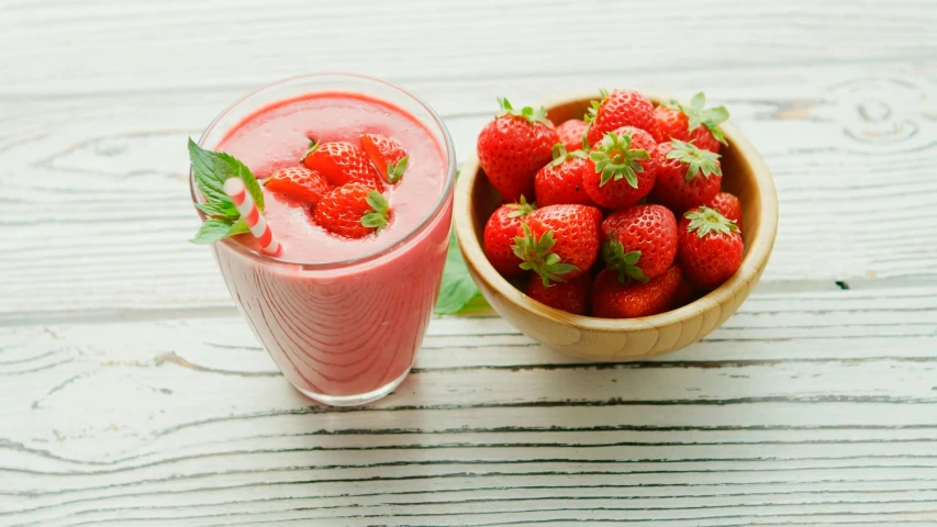 a bowl of strawberries with a glass of strawberry smoothie