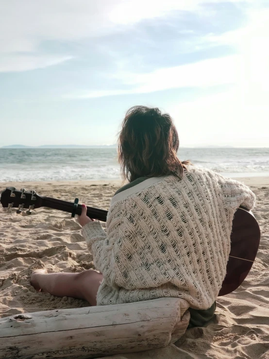 a woman sitting on the sand with a guitar