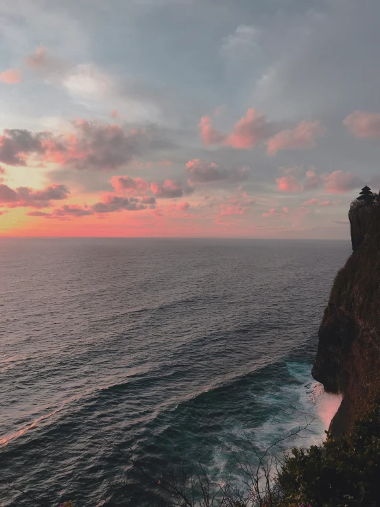 a person sitting on the cliff watching a sunset