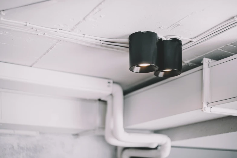 two black lamps hanging from the ceiling next to pipes