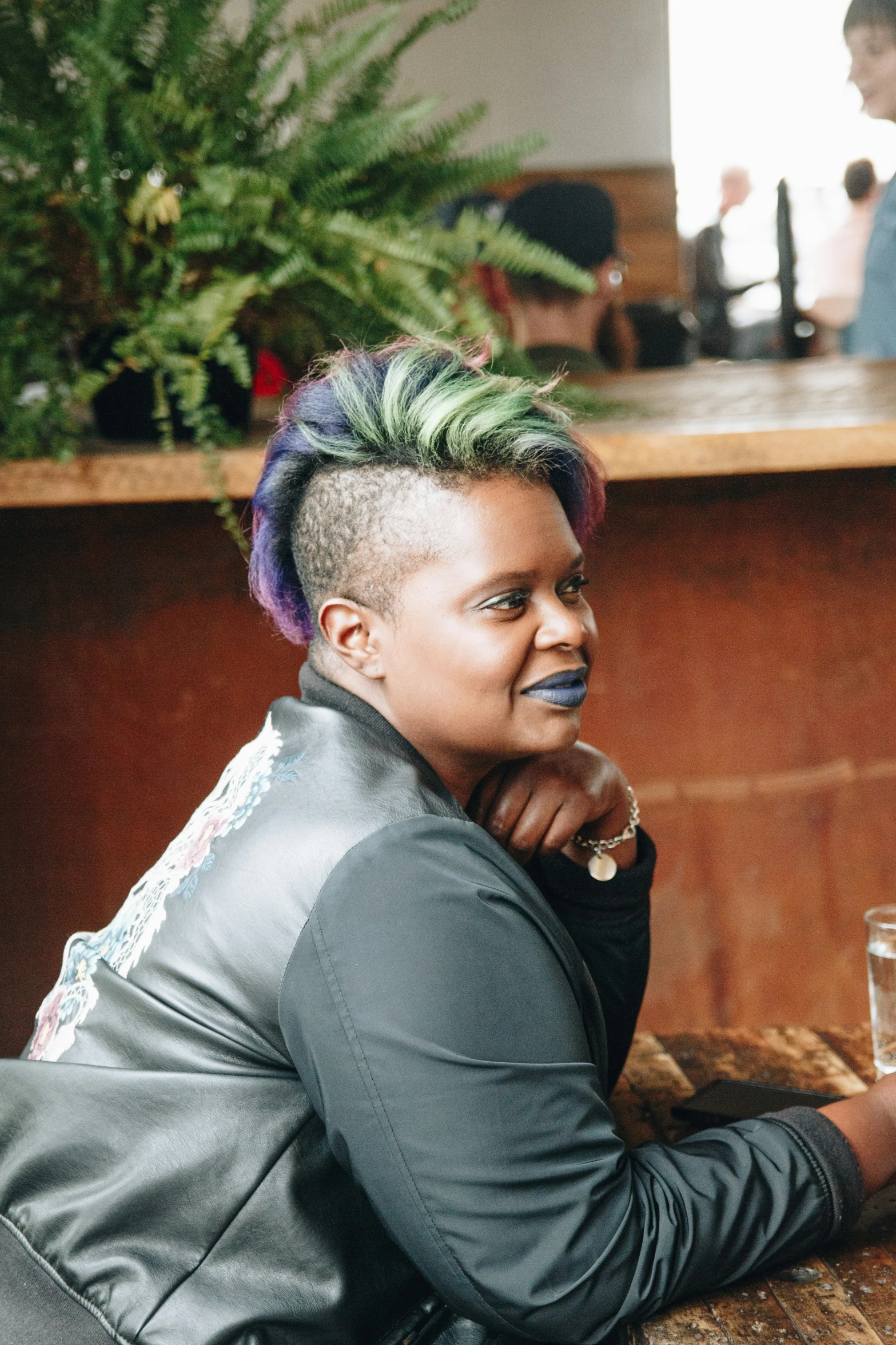 a smiling woman wearing blue hair sitting at a table