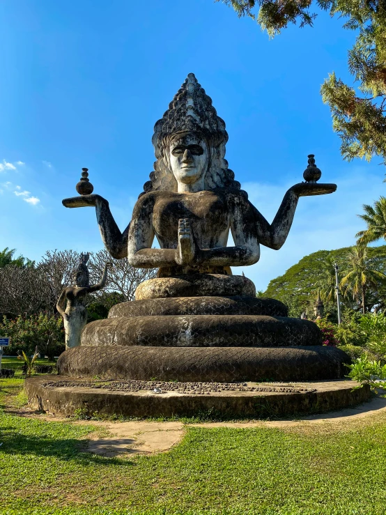 a statue of buddha holds two cups in the grass