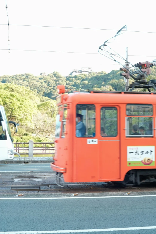 an orange trolley car stopped at a red crosswalk