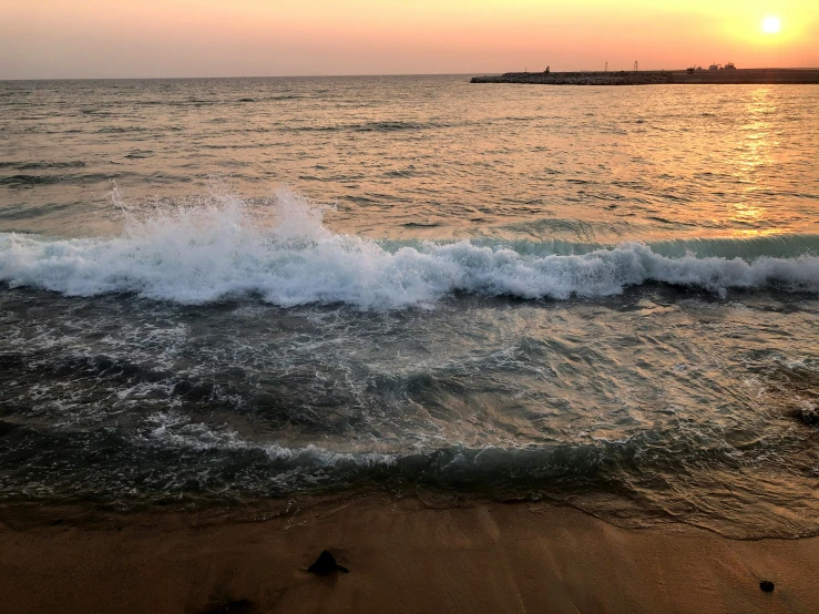 a beach scene with the sun going down and a distant ship in the distance