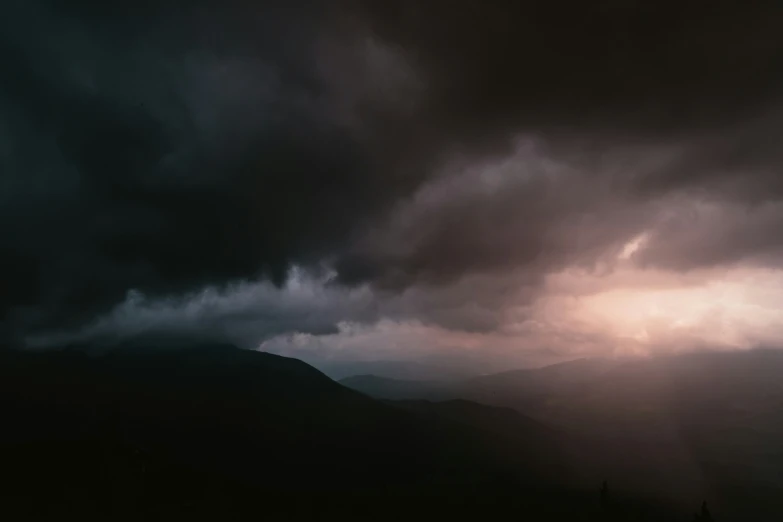 clouds, mountains and trees stand under a dark sky