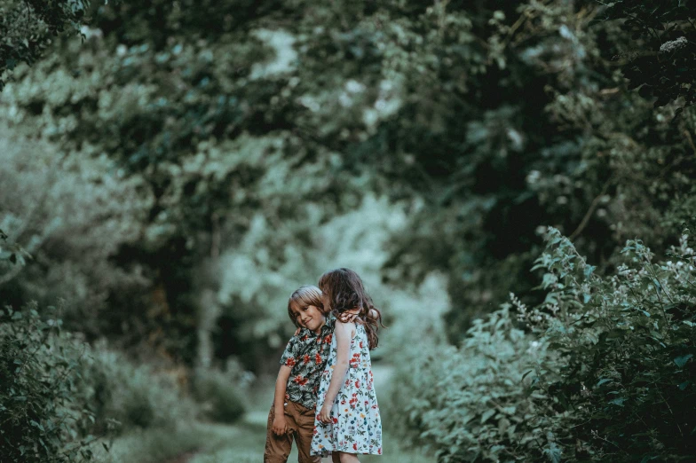 two children in the woods looking towards the ground