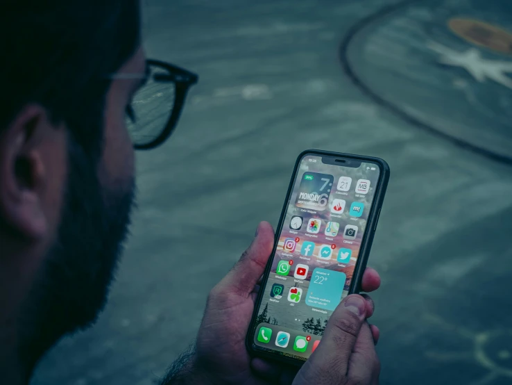 man wearing glasses holding up cell phone with icons on it