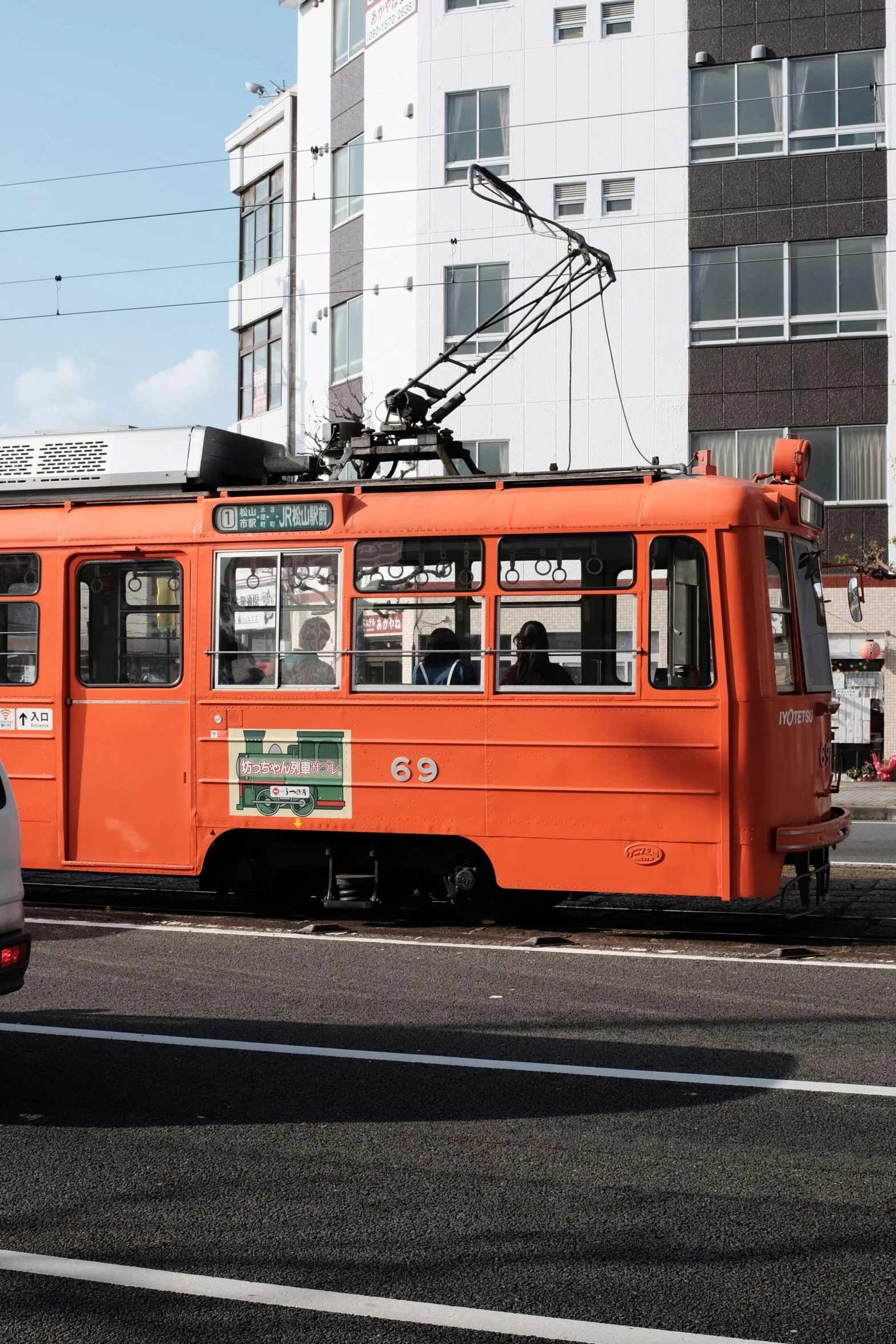 an orange trolly and white bus on street next to buildings