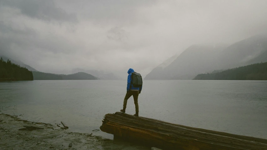 man standing on log on shore in rain