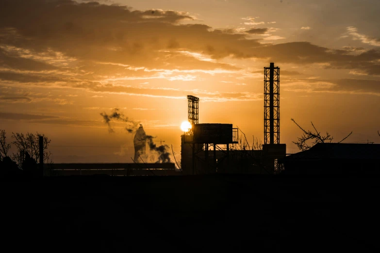 a factory at sunset with steam rising from stacks