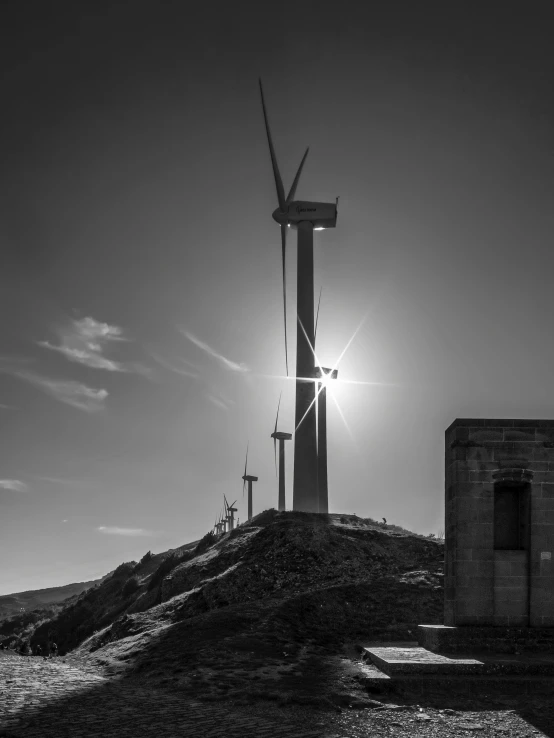 three windmills stand on a small hill near the sun