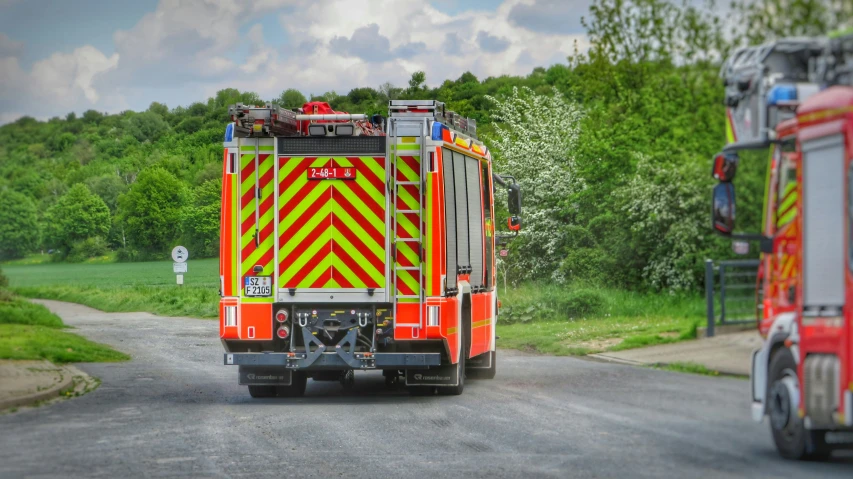 a red firetruck driving down a road near green grass