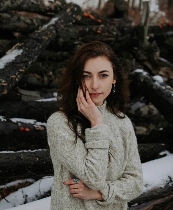 a woman stands in front of some logs in a snow covered forest