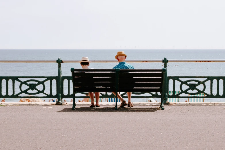 two people sit on a bench next to the ocean