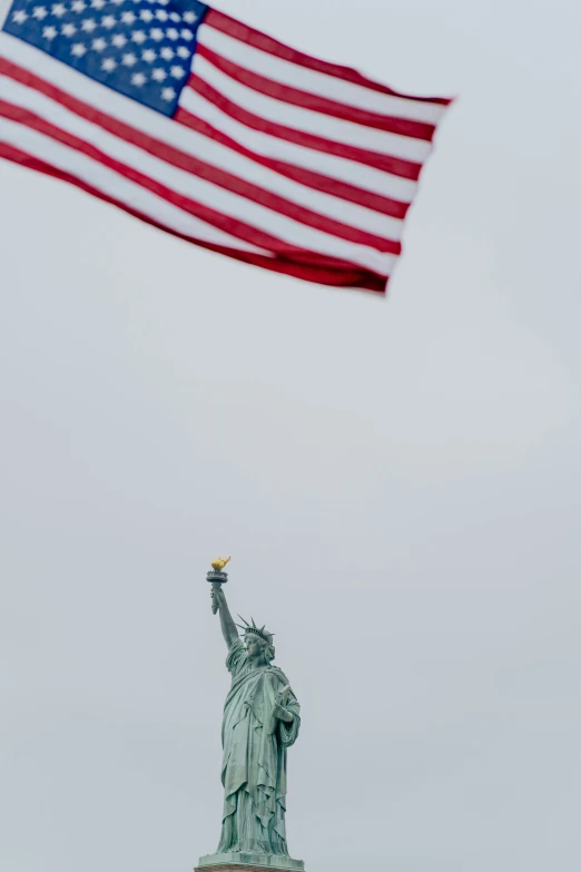 a flag flying over the statue of liberty on a cloudy day