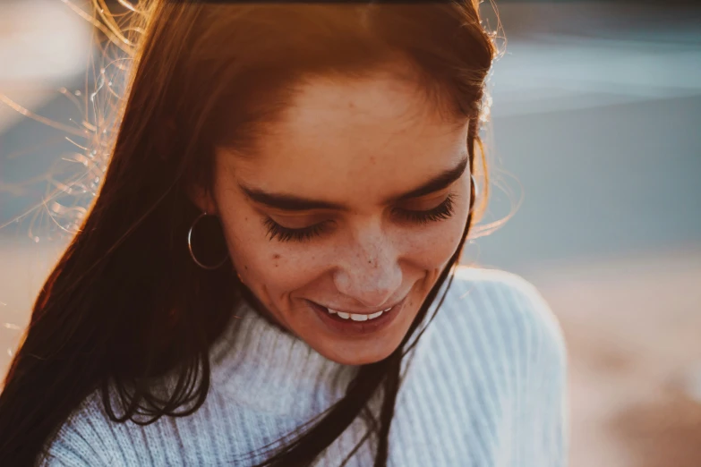 a girl in a sweater is smiling and looking at her cell phone