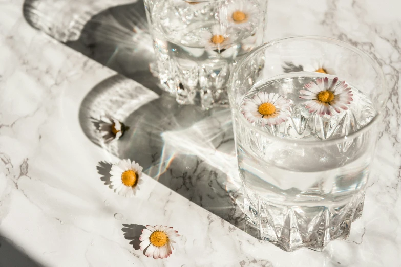 a small glass vase with daisies is next to a s glass