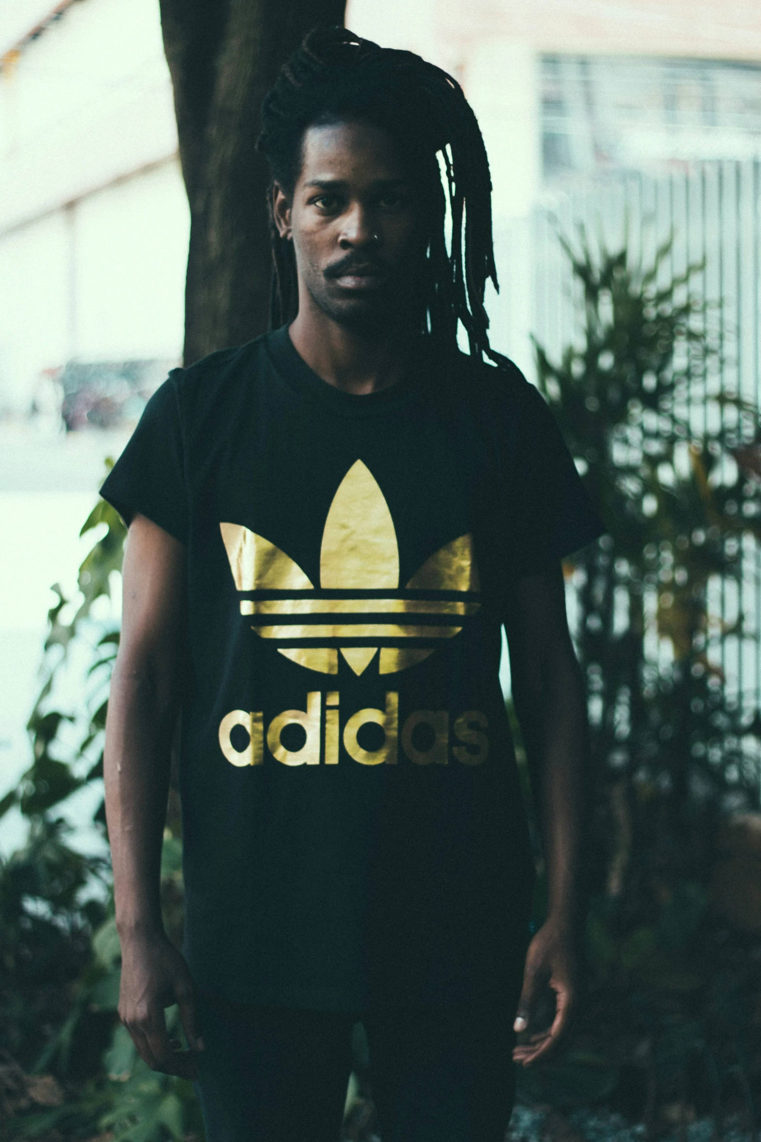 man in adidas shirt standing next to a tree