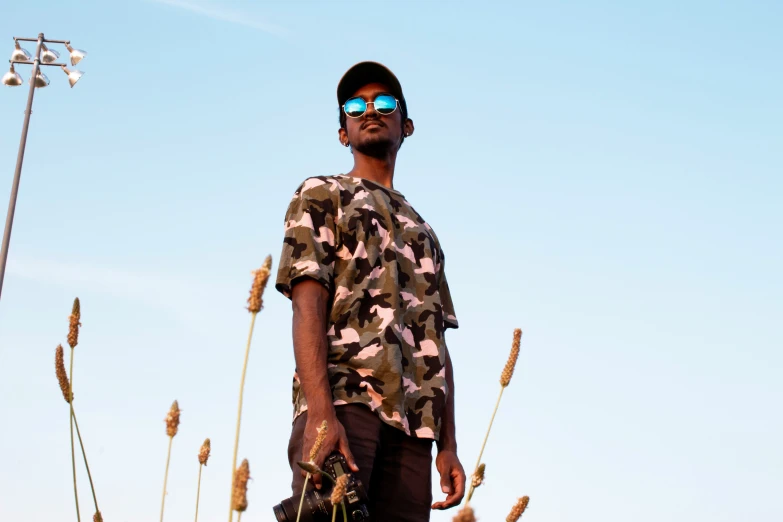 a man with sunglasses and camo shirt in front of tall grass