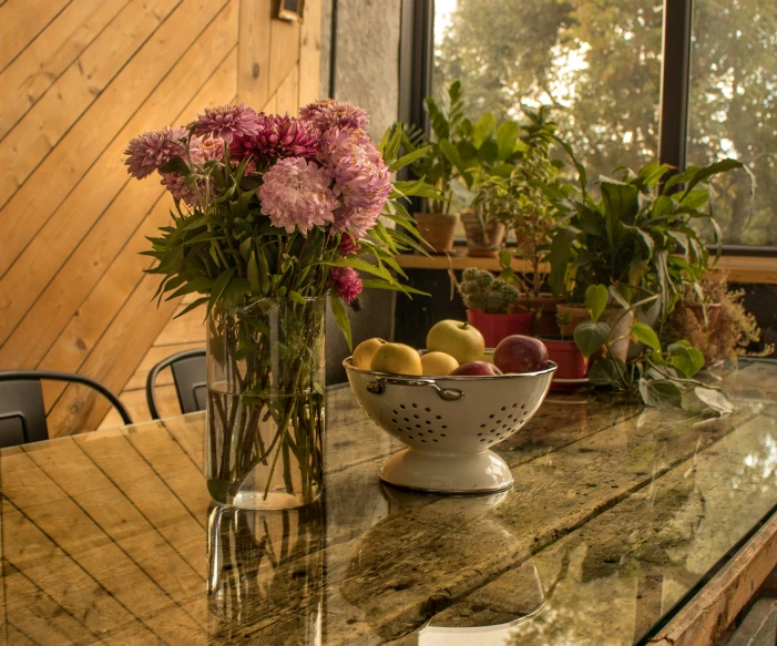 a table topped with a bowl of fruit next to a vase of flowers