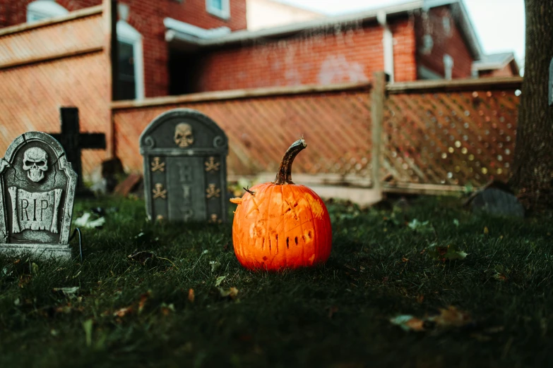 a pumpkin that is sitting in the grass next to a tombstone