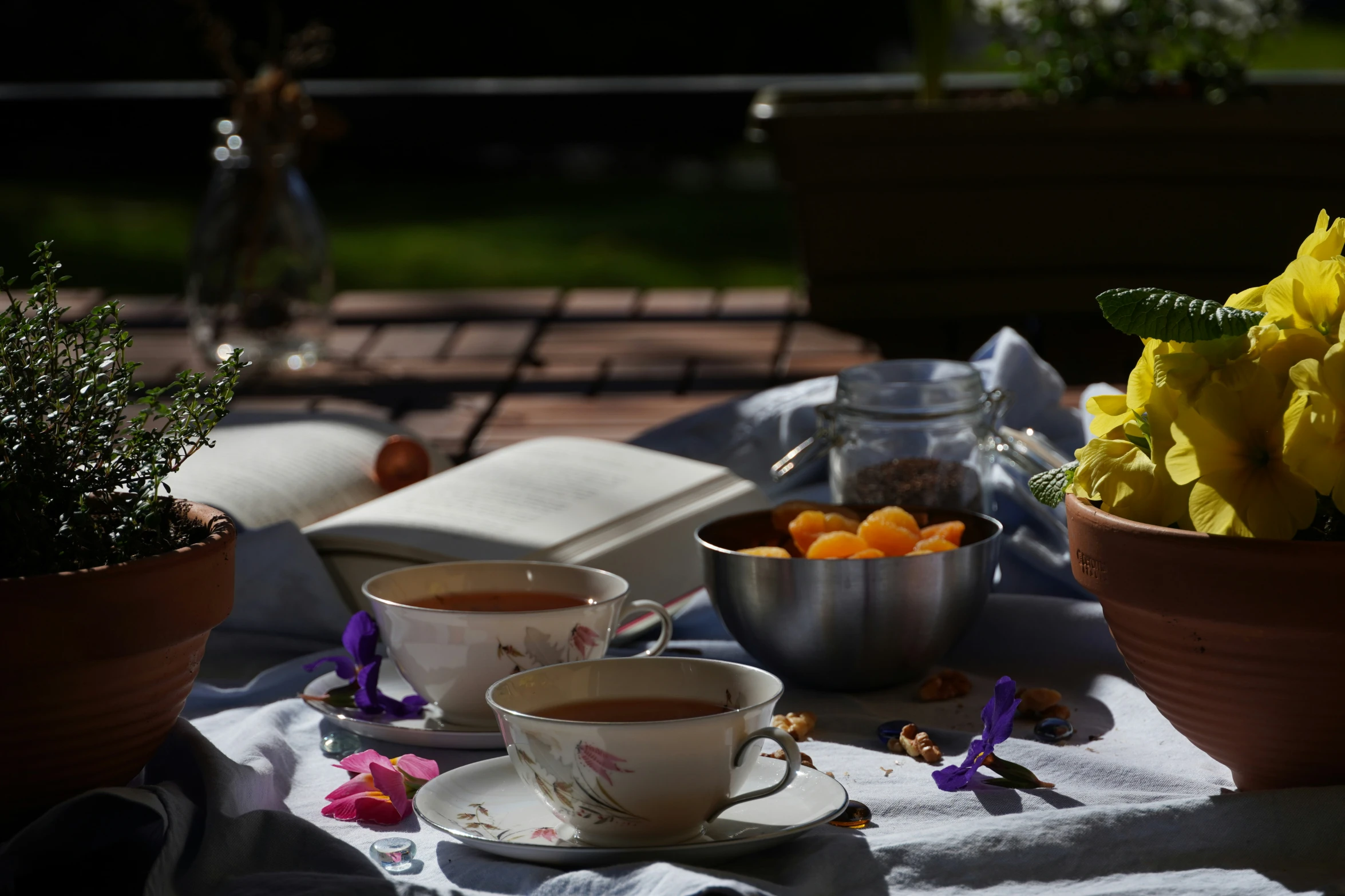 flowers in pots on a table with food, cups and saucers