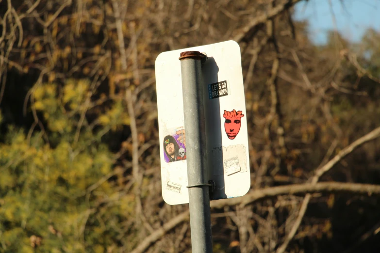 an upside down street sign with stickers and trees in the background