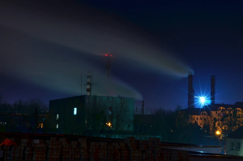 a factory and smoke stacks in the night with lights in the distance